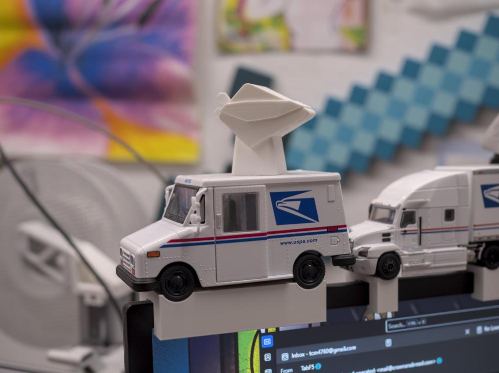 The tabling in all white, printed out sitting on top of a USPS model vehicle